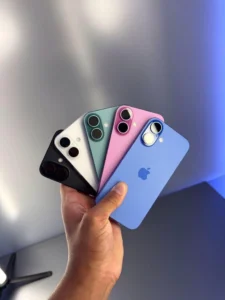 A hand holding five colorful iPhones in black, white, green, pink, and blue colors displayed in a fan arrangement."