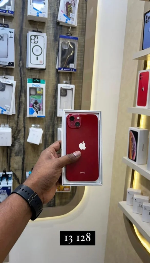 A person holding a red smartphone with dual cameras placed in its box.