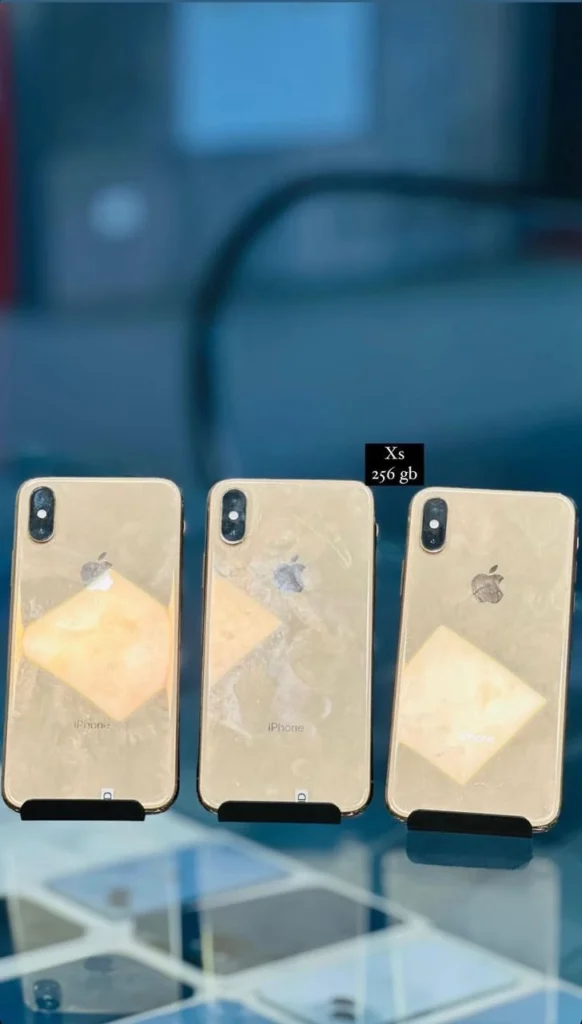 Three iPhone Xs models in gold color, each placed on individual stands with a label indicating 'Xs 256 GB' in the background.